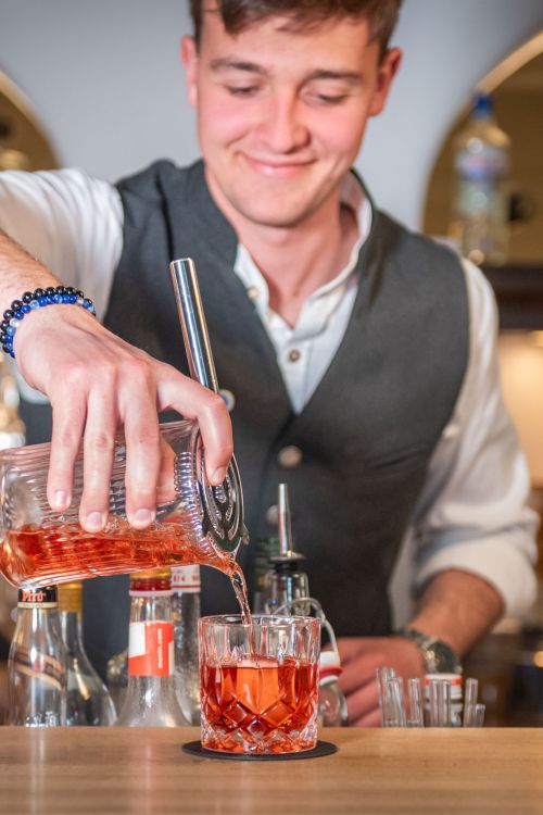 Barkeeper der Xaver Bar in Schliersee gießt zubereiteten Drink in ein Glas