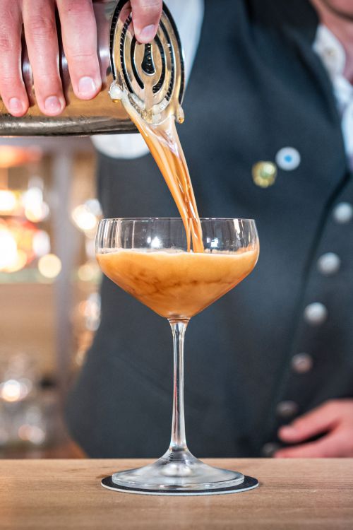 Barkeeper in der Bar Xaver in Schliersee gießt einen frisch zubereiteten Cocktail ins Glas
