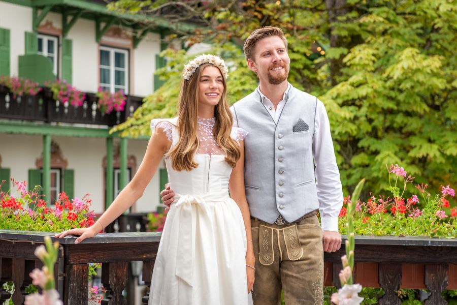 Happy bride and groom standing on a green balcony at the wedding venue at Lake Schliersee, enjoying the moment