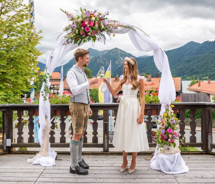 Bride and groom drinking champagne on the balcony of the wedding venue at Lake Schliersee with mountain views