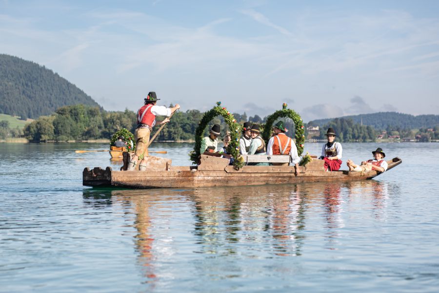 Trachtengruppe auf einer historischen Plätte vor der Bergkulisse am Schliersee
