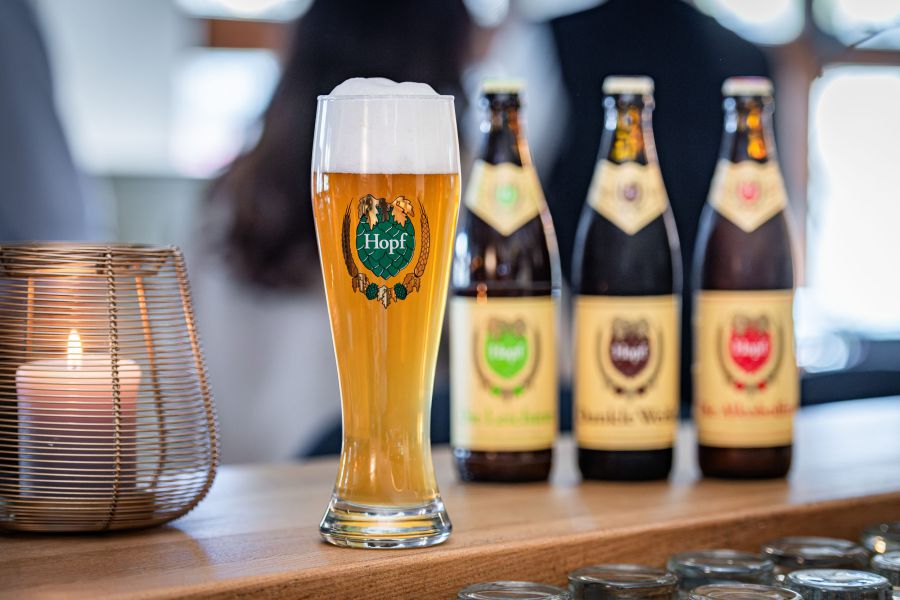 volles Weißbierglas, im Hintergrund drei Flaschen mit unterschiedlichen Weißbiersorten
