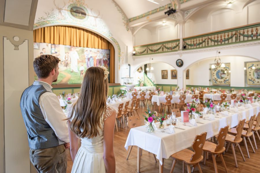 Brautpaar betrachtet zufrieden die festliche Tischdekoration im Hochzeitssaal des Bauerntheaters am Schliersee