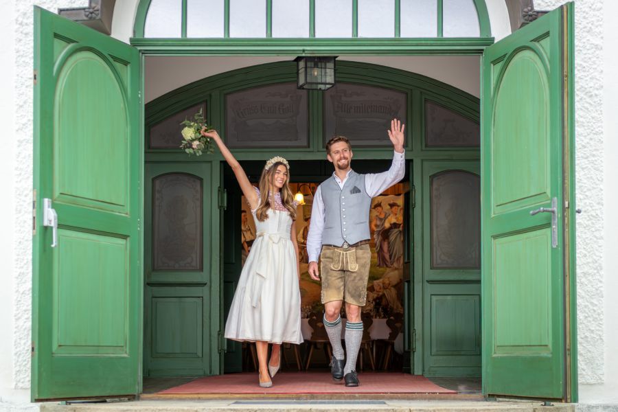 Bride and groom leaving the Bauerntheater wedding venue at Lake Schliersee and waving happily to their guests