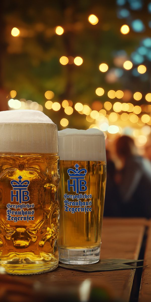 zwei Gläser mit Bier im Biergarten des Terofals in Schliersee, Abendstimmung mit Biergartenbeläuchtung unter der Kastanie