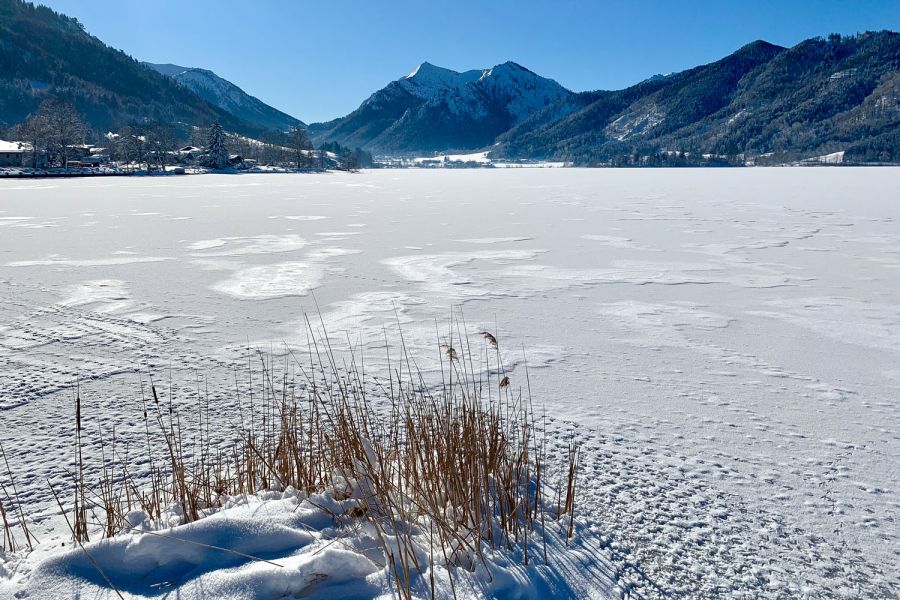 zugefrohrener Schliersee mit schneebedeckter Eisfläche, im Hintergrund die verschneiten Berge rund um Schliersee