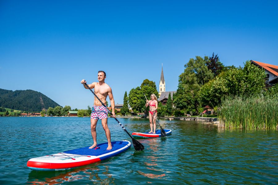 Guests of the Seeheimat in Schliersee paddling across Lake Schliersee on the property's own SUPs