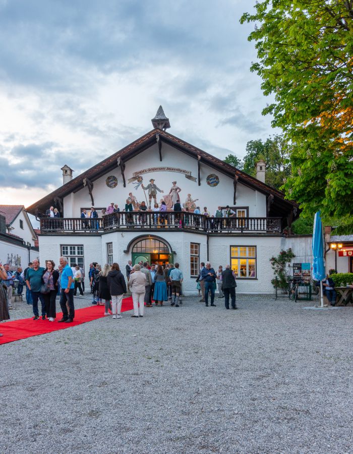 Besucher des Bauerntheaters in Schliersee warten vor dem historischen Gebäude auf den Einlass für die Theateraufführung