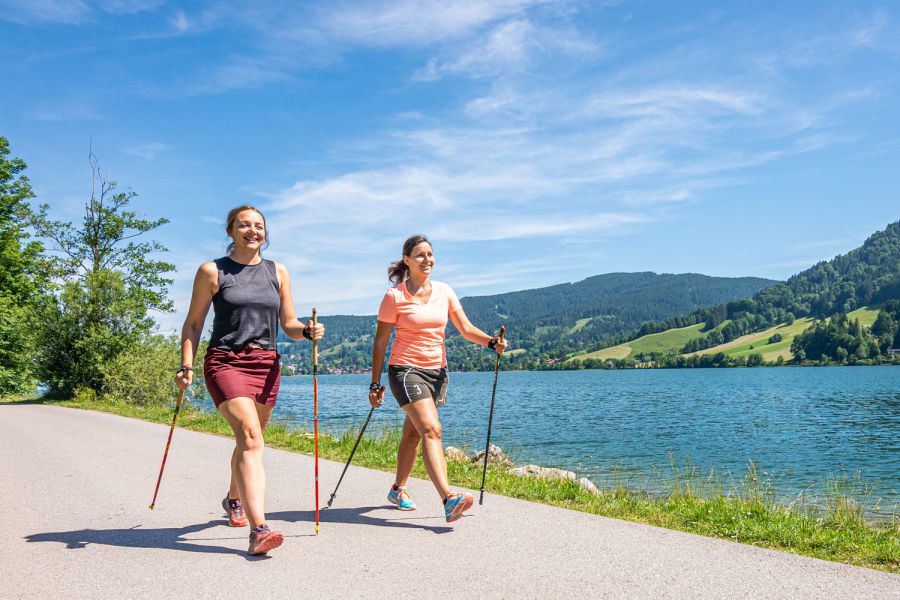 zwei Gäste des Terofals in Schliersee machen bei Sonnenschein am See Nordic Walking