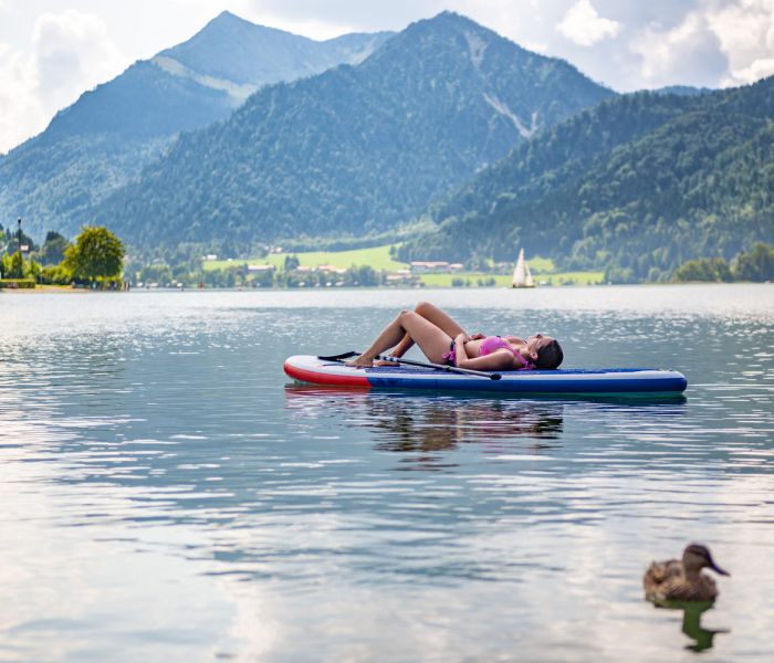 Gast der Seeheimat liegt auf einem SUP auf dem Schliersee und genießt die Sonne
