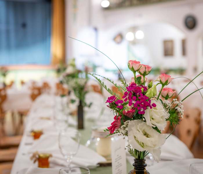 Für eine Hochzeit festlich gedeckter Tisch im Bauerntheater in Schliersee mit Blumenschmuck
